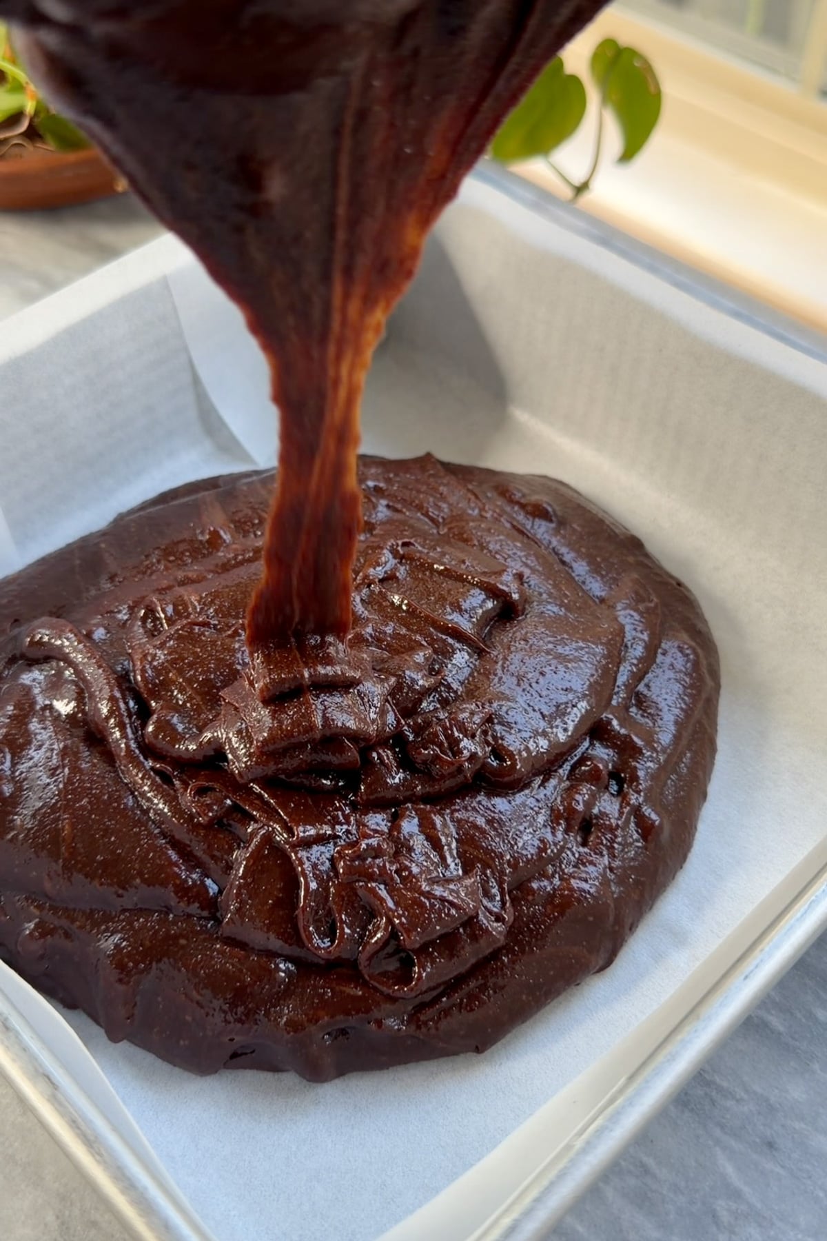 Brownie batter pouring into a lined 8x8 pan.