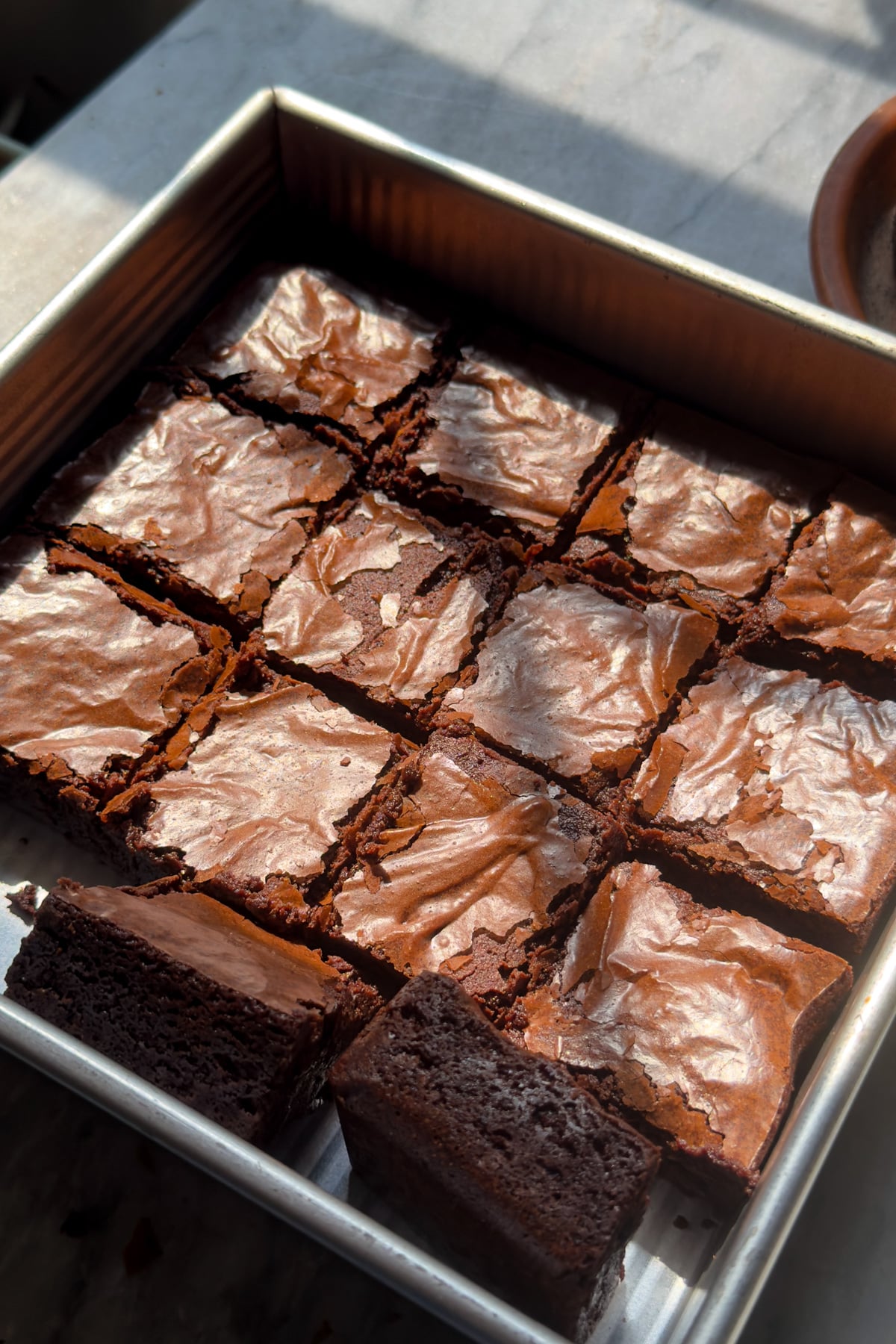 An 8x8 pan of crackly, shiny, fudgy brownies cut into squares.