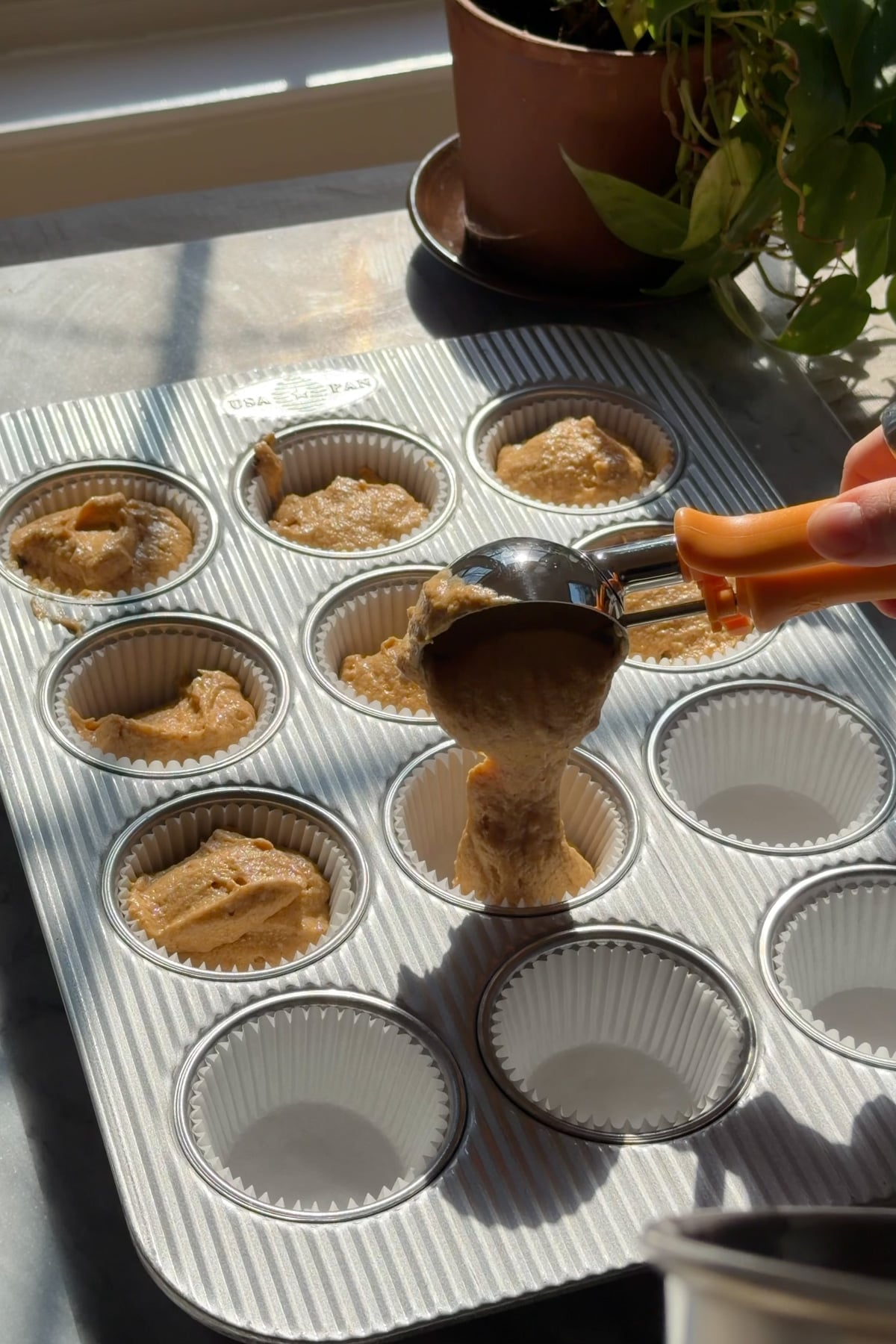 Pumpkin cupcake batter being scooped into a cupcake pan for pumpkin crunch cupcakes.