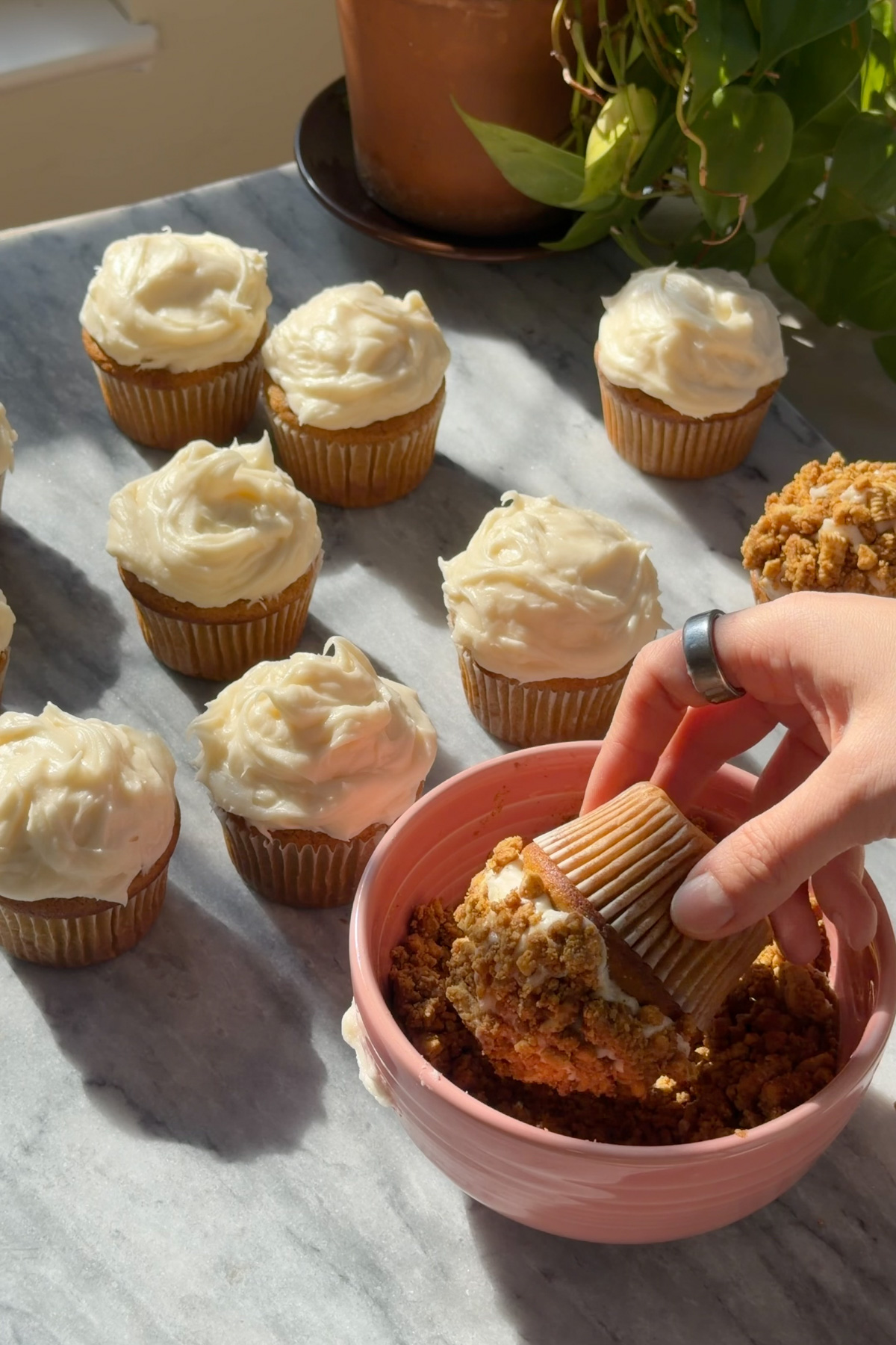 Pumpkin crunch cupcakes with cream cheese frosting being rolled in pumpkin crunch topping.