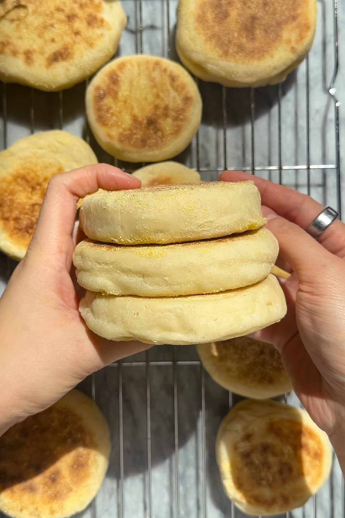 Two hands holding three sourdough discard English muffins stacked on top of each other.
