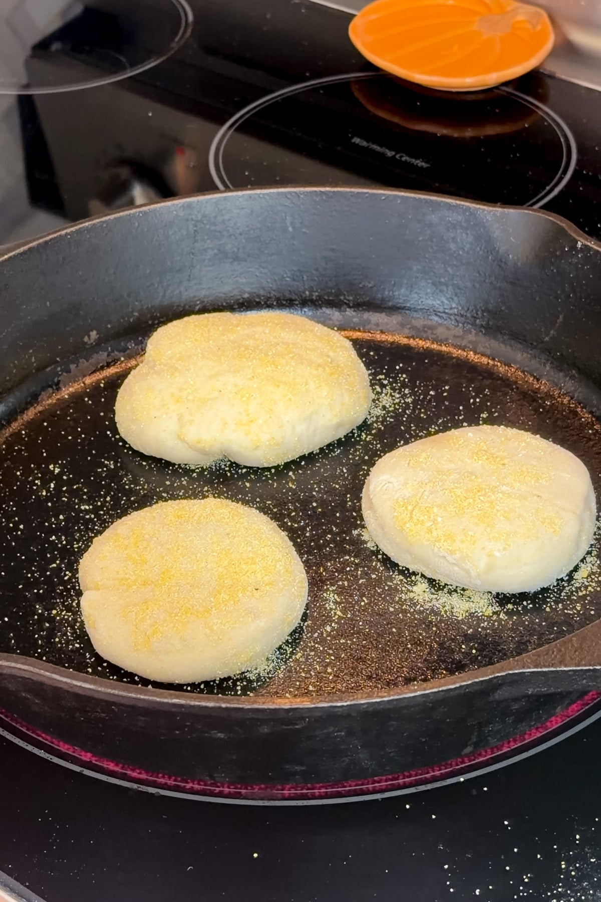 Sourdough discard English muffins cooking in a cast iron pan.